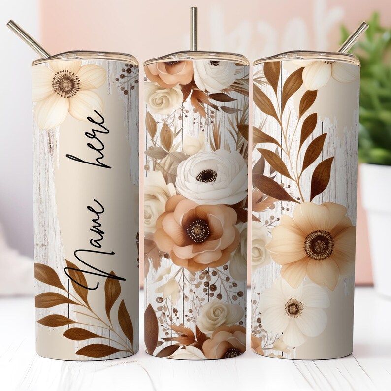May include: Three stainless steel tumblers with a white woodgrain background and a floral design in shades of brown and cream. The tumbler on the left has the text "Name here" on it.