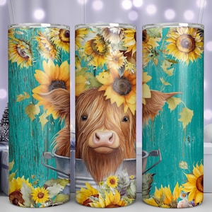 May include: A brown and white Highland cow with a sunflower crown peeks out of a metal bucket. The cow is surrounded by sunflowers and leaves on a turquoise wooden background.