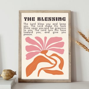 May include: A framed art print with the text "THE BLESSING" and a floral design in pink and orange. The print is displayed on a white shelf with a vase of wheat and a book.