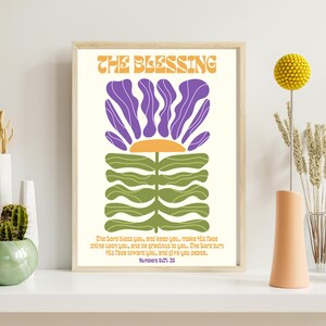 Könnte beinhalten: Ein druckbarer Wandkunstdruck mit einem grünen und violetten Blumendesign und dem Text "THE BLESSING" in einer Retro-Schriftart. Der Text unter der Blume lautet: "Der Herr segne dich und behüte dich, er lasse sein Angesicht leuchten über dir und sei dir gnädig. Der Herr wende sein Angesicht zu dir und gebe dir Frieden. Numeri 6:24-26"
