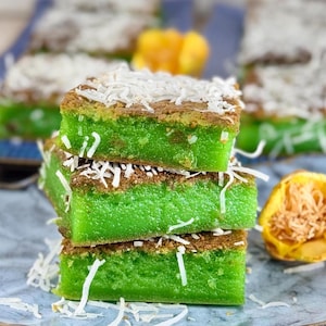 May include: A stack of three green and brown coconut cake squares on a blue plate. The cake is topped with shredded coconut.