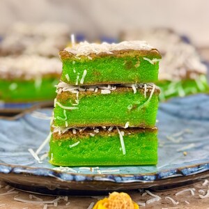May include: A stack of three green and brown sponge cakes topped with shredded coconut. The cakes are on a blue and white patterned plate.