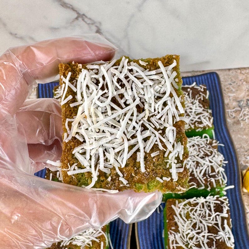 May include: A close-up of a green cake topped with shredded coconut. The cake is cut into squares and is sitting on a blue and white plate.
