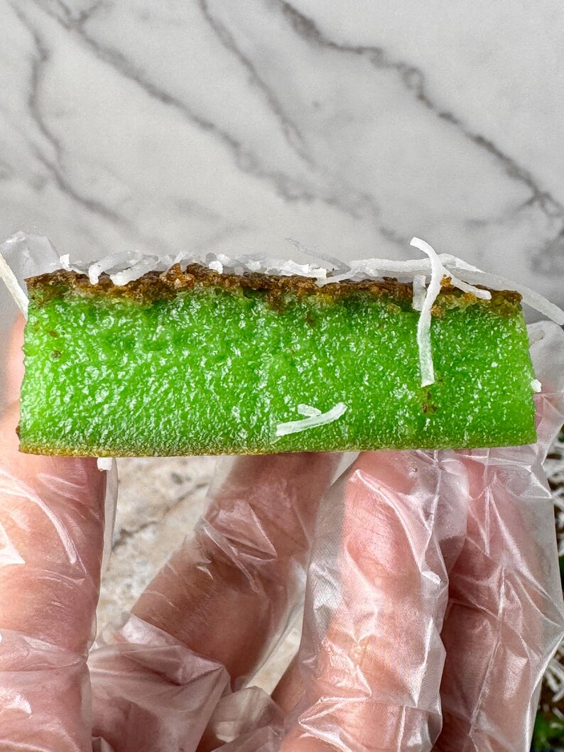 May include: A green and brown cake topped with shredded coconut. The cake is being held by a gloved hand.