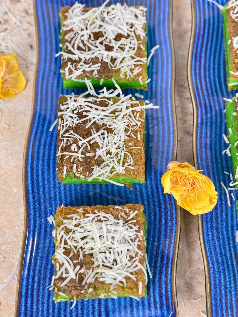 May include: Three squares of green cake topped with shredded coconut on a blue and white striped plate.