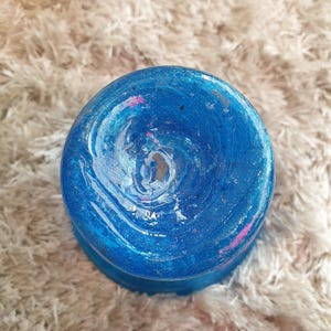 May include: A round, blue decorative object with a swirling pattern of white, pink, and blue paint. The object has a glossy finish and sits on a fluffy, light-colored surface. The object's design is reminiscent of a galaxy.