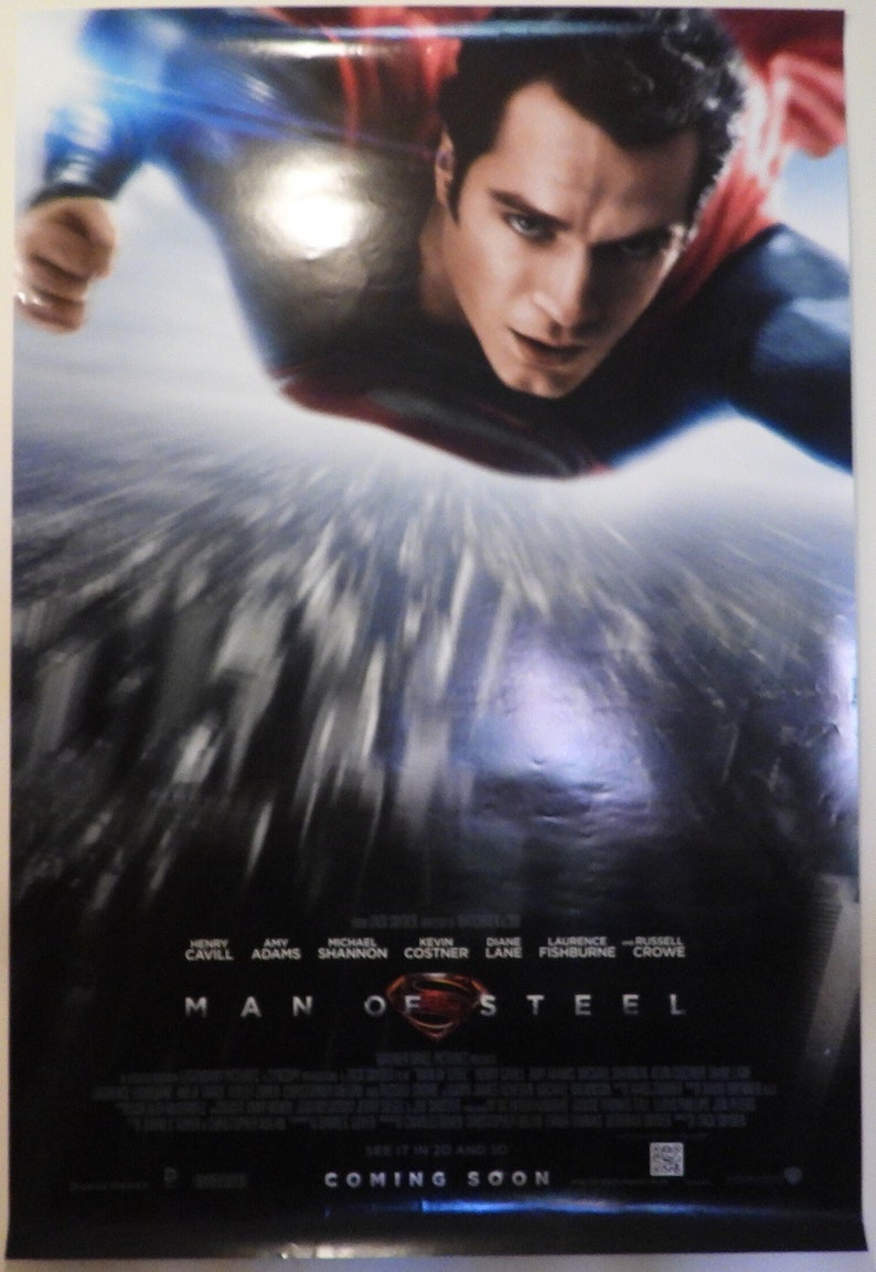 Może przedstawiać: Plakat filmowy do filmu "Człowiek ze stali" z Henrym Cavillem jako Supermanem lecącym w powietrzu. Plakat ma ciemnoniebieskie tło z rozmytym obrazem miasta w tle. Tekst "Człowiek ze stali" znajduje się dużymi białymi literami na dole plakatu.