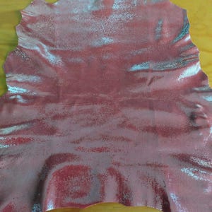 May include: A piece of red leather with a silver shimmer finish. The leather has a textured surface and is slightly wrinkled.