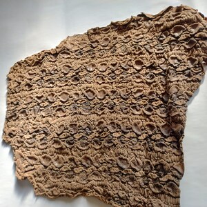 May include: A brown textured fabric with a raised pattern resembling scales. The fabric is wrinkled and has a slightly uneven surface.