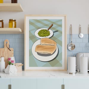 Puede incluir: Una impresión enmarcada que presenta una naturaleza muerta de comida. Dos mitades de un sándwich están en un plato blanco, y un plato pequeño contiene una pasta verde con una cuchara. El fondo tiene un patrón de cuadros.