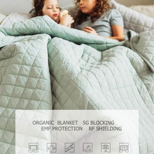 Puede incluir: Dos niños están tumbados bajo una manta acolchada de color verde claro. La manta se anuncia como una manta orgánica que bloquea las señales 5G y RF. El texto "SWAN HERO YOUR OFFLINE LUXURY" está en la parte superior de la imagen.