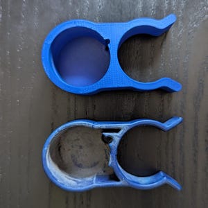 Peut inclure: Deux clips en plastique bleus, l'un au-dessus de l'autre, sont présentés sur un fond sombre. Le clip supérieur est bleu vif, tandis que le clip inférieur est bleu délavé. Chaque clip a une ouverture circulaire et des bras incurvés.