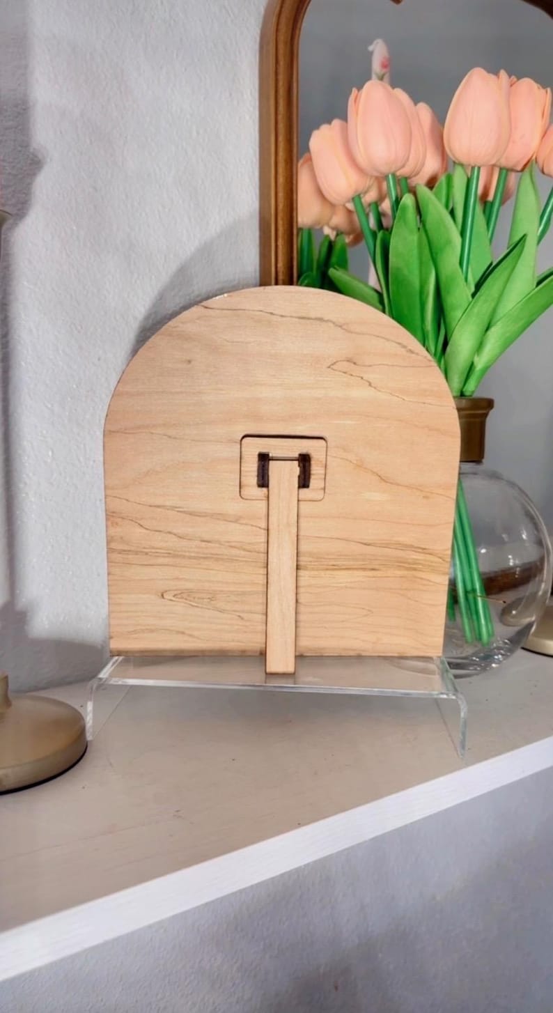 K&ouml;nnte beinhalten: Ein Holzbildrahmen mit hellbrauner Oberfl&auml;che und einem St&auml;nder auf der R&uuml;ckseite. Der Rahmen ist bogenf&ouml;rmig und hat ein schlichtes Design.