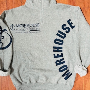 May include: Gray sweatshirt with a black logo that says "Morehouse School of Medicine" and "Doctor of Health Administration". The word "Morehouse" is also printed in black on the right sleeve in a curved arc.