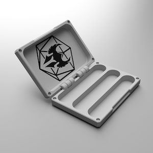 May include: A light grey, open, rectangular case with a hinged lid. The lid features a black graphic of a stylized dragon within a geometric shape. The interior has two long, curved compartments. The case is designed for small items.