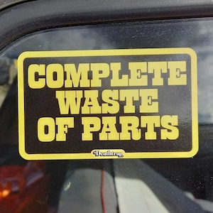 以下が含まれることがあります： 「COMPLETE WASTE OF PARTS」というテキストと、その下に小さく「Deathtrap」という単語が書かれた、黄色と黒のステッカーです。