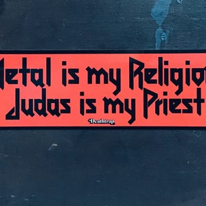Op de afbeelding: Een rode sticker met zwarte tekst die "Metal is my Religion Judas is my Priest" zegt met de woorden "Deathrap" in een kleiner lettertype onder de tekst.
