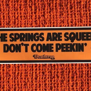 May include: Orange and black sticker with the text "IF THE SPRINGS ARE SQUEEKIN' DON'T COME PEEKIN'" and the text "DeathTrap" in a smaller font.