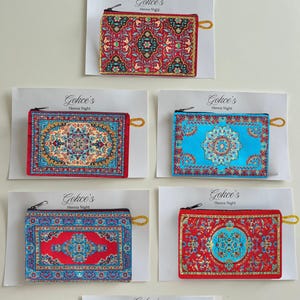 Peut inclure: Cinq pochettes rectangulaires à fermeture éclair avec des motifs de tapis tissés complexes et colorés. Chaque pochette est fixée sur une carte blanche marquée "Gokce's Henna Night". Les motifs incluent des fleurs rouges, bleues et turquoise.