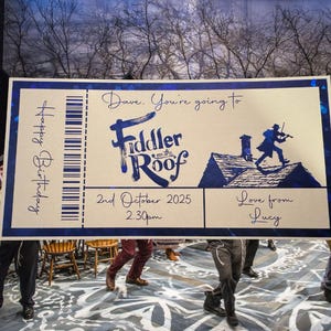 May include: A large, light brown ticket with blue text and a blue border. The ticket says "Happy Birthday" and "Dave. You're going to Fiddler on the Roof" with the date "2nd October 2025" and time "2:30pm". The ticket also says "Love from Lucy".