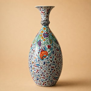 May include: A tall, decorative ceramic vase with a white base and a colorful floral pattern. The vase features a slender neck, a bulbous body, and a flared rim. The floral design includes orange, blue, purple, and yellow flowers and green leaves.