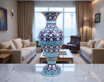 May include: A tall, decorative vase with a flared top and base. The vase features a dark blue background with white floral patterns and turquoise accents. The vase is displayed on a marble surface.