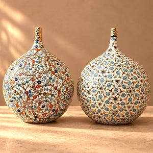 Può includere: Due vasi sferici in ceramica con colli stretti e bordi dorati. Il vaso a sinistra presenta un denso motivo floreale multicolore in rosso, blu e verde. Il vaso a destra mostra una griglia geometrica con piccoli fiori di colore blu.
