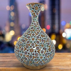 Pu&ograve; includere: Un vaso bulboso con collo stretto e bordo svasato, caratterizzato da un colore di base azzurro decorato con un intricato motivo ripetitivo di piccoli fiori rosa, steli verdi e accenti color oro su tutta la superficie esterna.