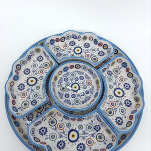 Peut inclure: Un plat de service en c&eacute;ramique blanche avec un bord bleu et un motif floral bleu et blanc. Le plat comporte cinq petits bols, chacun avec un bord bleu et un motif floral bleu et blanc. Les bols sont dispos&eacute;s en cercle autour du centre du plat. Les bols ont un motif floral bleu et blanc avec un &oelig;il jaune au centre de chaque fleur.