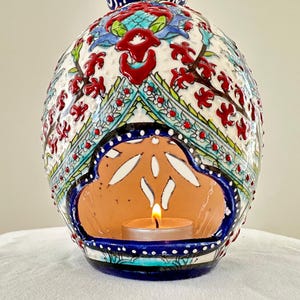 May include: A ceramic candle holder with intricate blue, red, and white floral designs. The holder has a cutout in the shape of a cloud, where a small tea light candle sits.