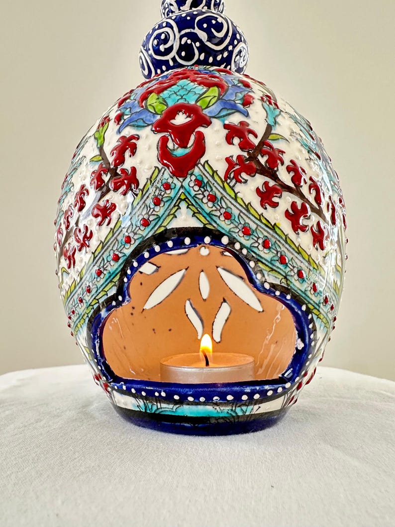 May include: A ceramic candle holder with intricate blue, red, and white floral designs. The holder has a cutout in the shape of a cloud, where a small tea light candle sits.