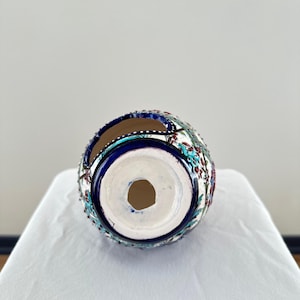 May include: A white ceramic vase with a blue and red floral pattern. The vase has a round shape and a hole in the bottom for drainage.