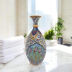 Könnte beinhalten: Eine blaue und weiße Keramikvase mit einem Blumendesign. Die Vase hat einen schmalen Hals und einen breiten Boden. Das Blumendesign zeigt Tulpen, Blätter und andere Blumen. Die Vase ist mit goldenen Akzenten verziert.