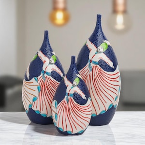 Puede incluir: Conjunto de tres jarrones decorativos. Los jarrones tienen un fondo azul marino texturizado y presentan un diseño de figuras de derviches giratorios en blanco y rojo, con detalles verdes y azules. Los jarrones son de diferentes tamaños.