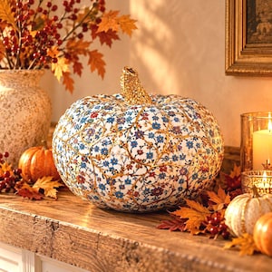 May include: A decorative pumpkin featuring a white base with an intricate pattern of blue, red, and purple flowers connected by gold vines. The pumpkin has a textured gold stem and a rounded, ribbed shape, serving as a centrepiece for seasonal decor.