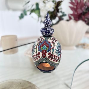 May include: A white ceramic candle holder with a blue and red floral design. The holder has a round shape with a pointed top and a small opening for a candle.