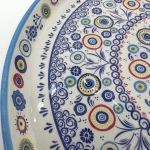 Peut inclure: Un plateau de service en c&eacute;ramique blanche avec un bord bleu et un motif d&eacute;coratif de cercles et de volutes bleus, jaunes et rouges. Le motif comprend un motif r&eacute;p&eacute;titif du symbole du mauvais &oelig;il.