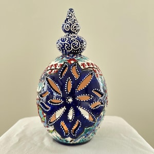 May include: A blue and white ceramic candle holder with intricate floral designs and a cut-out pattern. The holder has a domed top with a finial.