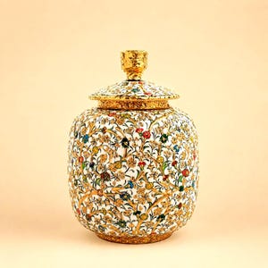 Può includere: Un barattolo decorativo con coperchio caratterizzato da una base bianca decorata con intricati filigrani dorati e motivi floreali colorati in rosso, blu, giallo e verde. Il barattolo ha un corpo arrotondato e un coperchio dorato con pomello.
