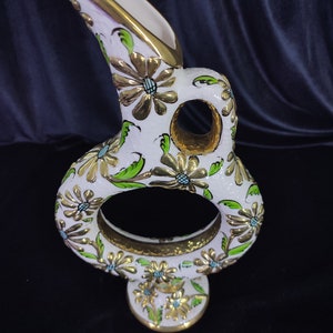 以下が含まれることがあります： 金と緑の花柄が施された白い陶器の花瓶。花瓶は、上部に大きな開口部、下部に小さな開口部を持つユニークな形をしています。