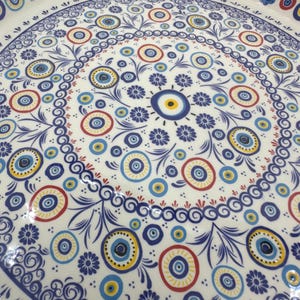Peut inclure: Un plateau de service en c&eacute;ramique blanche avec un motif floral bleu et blanc et un motif r&eacute;p&eacute;t&eacute; d'yeux bleus avec des centres jaunes. Le plateau a une bordure bleue.