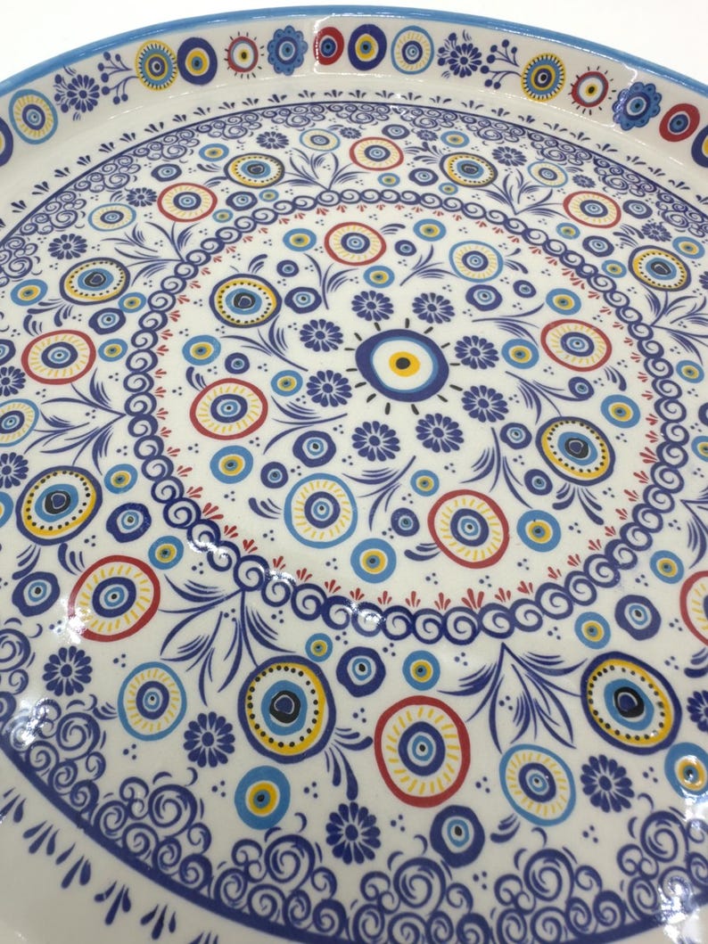 Peut inclure: Un plateau de service en c&eacute;ramique blanche avec un motif floral bleu et blanc et un motif r&eacute;p&eacute;t&eacute; d'yeux bleus avec des centres jaunes. Le plateau a une bordure bleue.