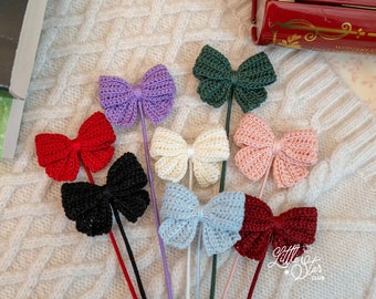 May include: A set of eight crocheted bows in various colors, including red, pink, white, blue, green, purple, and black. The bows are attached to thin sticks and are arranged on a white knitted surface.