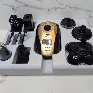 May include: A white foam tray containing a black and gold electric shaver and various attachments. The shaver has a digital display and the letter "F" on the front. The attachments include a nose trimmer, a detail trimmer, and a shaving head.