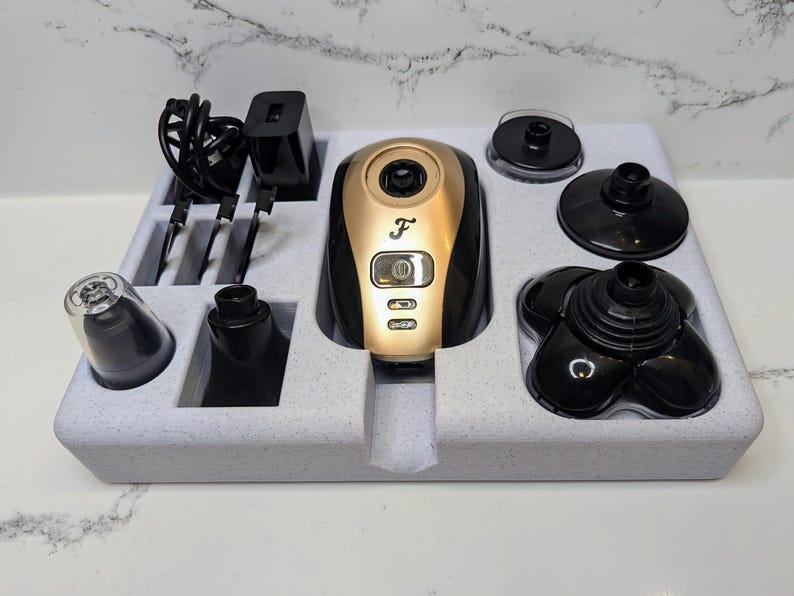 May include: A white foam tray containing a black and gold electric shaver and various attachments. The shaver has a digital display and the letter "F" on the front. The attachments include a nose trimmer, a detail trimmer, and a shaving head.