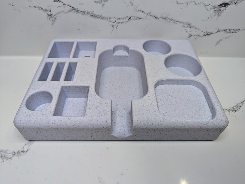 May include: A white, speckled, rectangular tray with multiple compartments of varying sizes. The tray has a large, oval-shaped cutout in the centre.