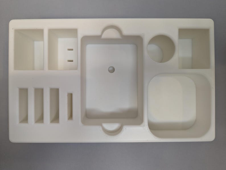 Puede incluir: Bandeja organizadora de pl&aacute;stico blanco con m&uacute;ltiples compartimentos de diferentes tama&ntilde;os. La bandeja tiene un compartimento rectangular grande en el centro, un compartimento rectangular m&aacute;s peque&ntilde;o a la derecha y un compartimento circular en la parte superior derecha. Hay cinco compartimentos rectangulares m&aacute;s peque&ntilde;os en el lado izquierdo de la bandeja.