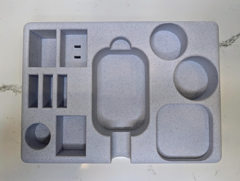 May include: A grey foam organiser with multiple compartments. The organiser has a large rectangular compartment in the centre, a smaller rectangular compartment to the left, and three round compartments to the right.
