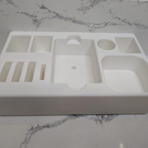 Puede incluir: Organizador de pl&aacute;stico blanco con m&uacute;ltiples compartimentos de diferentes tama&ntilde;os. El organizador tiene una forma rectangular y es ideal para guardar objetos peque&ntilde;os.