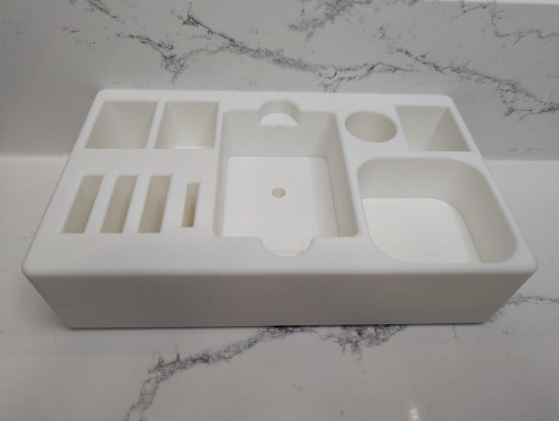 Puede incluir: Organizador de pl&aacute;stico blanco con m&uacute;ltiples compartimentos de diferentes tama&ntilde;os. El organizador tiene una forma rectangular y es ideal para guardar objetos peque&ntilde;os.